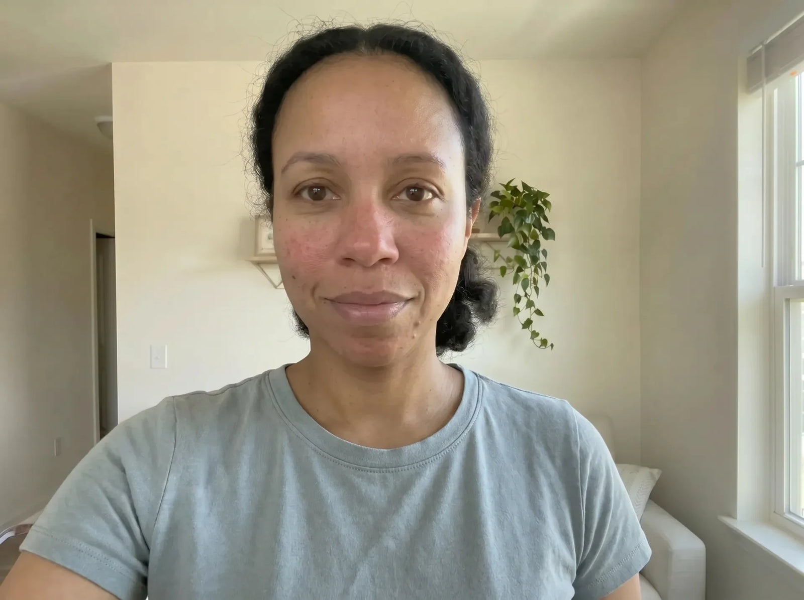 Woman with clear, even-toned skin wearing a light blue t-shirt, hair pulled back, photographed indoors with natural light