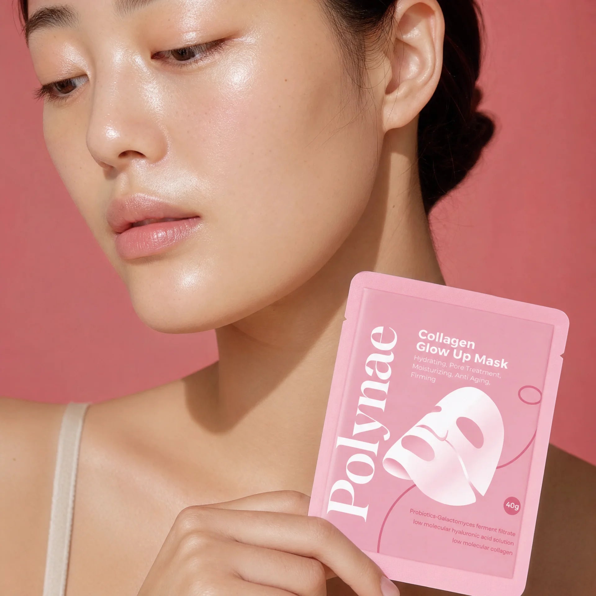 Close-up of a woman with luminous, hydrated skin holding a pink Polynae Collagen Glow Up Mask packet against a rose background