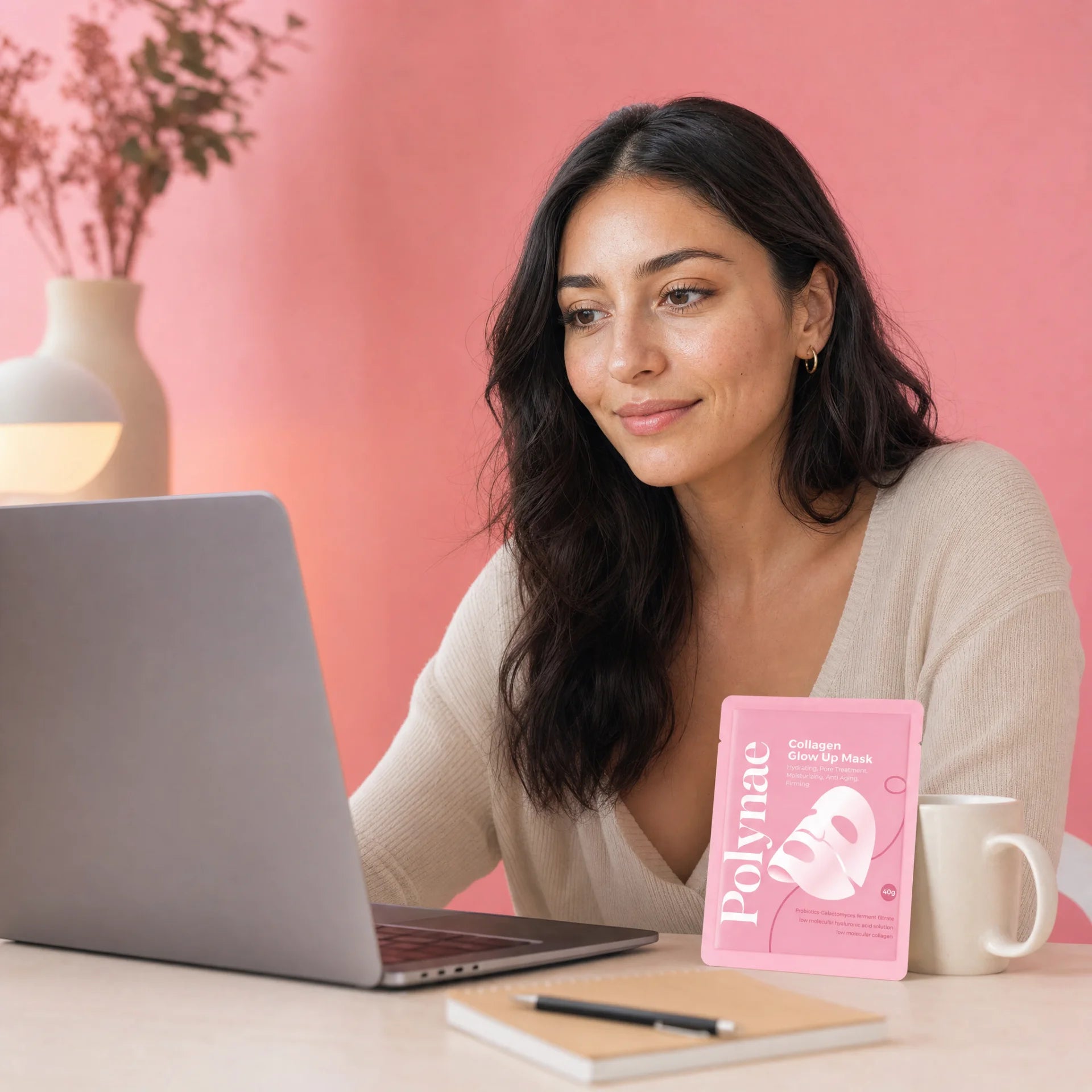 Woman sitting at a desk with a laptop and a Polynae Collagen Glow Up Mask packet placed beside a coffee mug and notebook