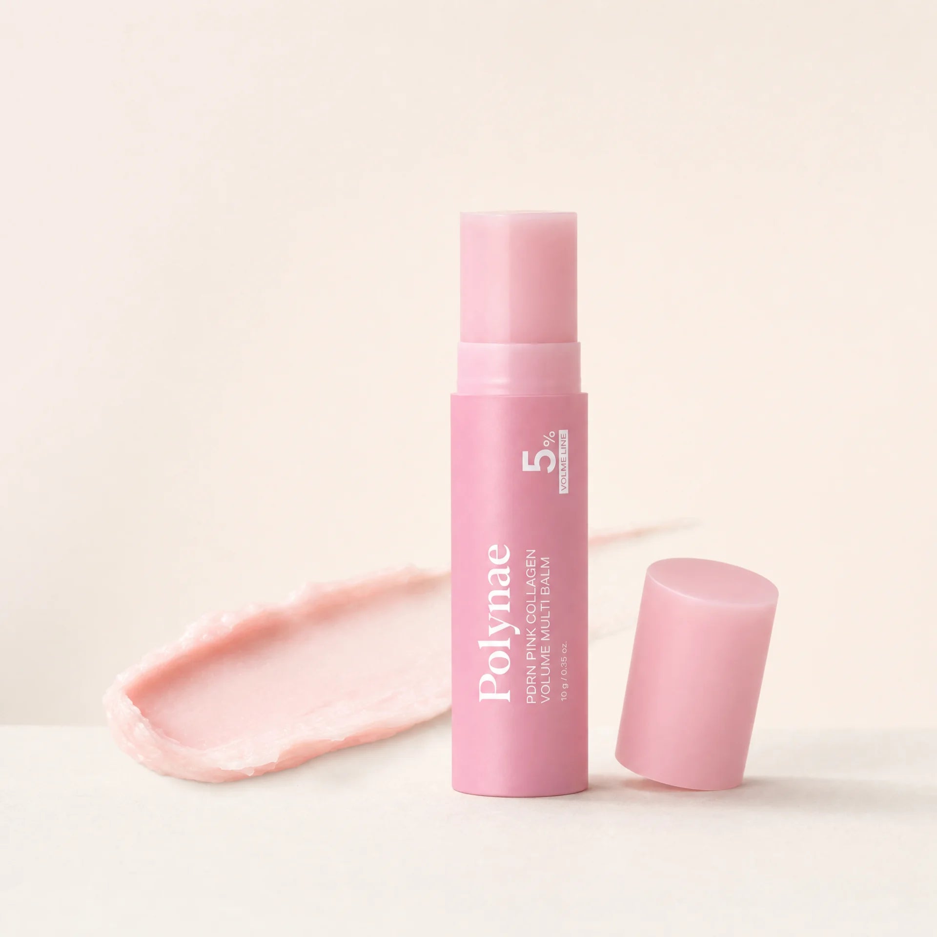 Polynae PDRN Pink Collagen Volume Multi Balm stick in pink packaging standing upright with cap removed beside it and a pink balm swatch on a cream surface