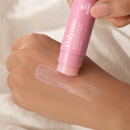 Close-up of the Polynae balm stick being swiped across the back of a hand with a sheer pink glassy texture trail visible on medium-toned skin