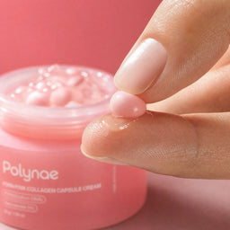 Fingertip holding a single pink collagen capsule bead from Polynae PDRN Pink Collagen Capsule Cream, with the open jar visible in the soft-focus background