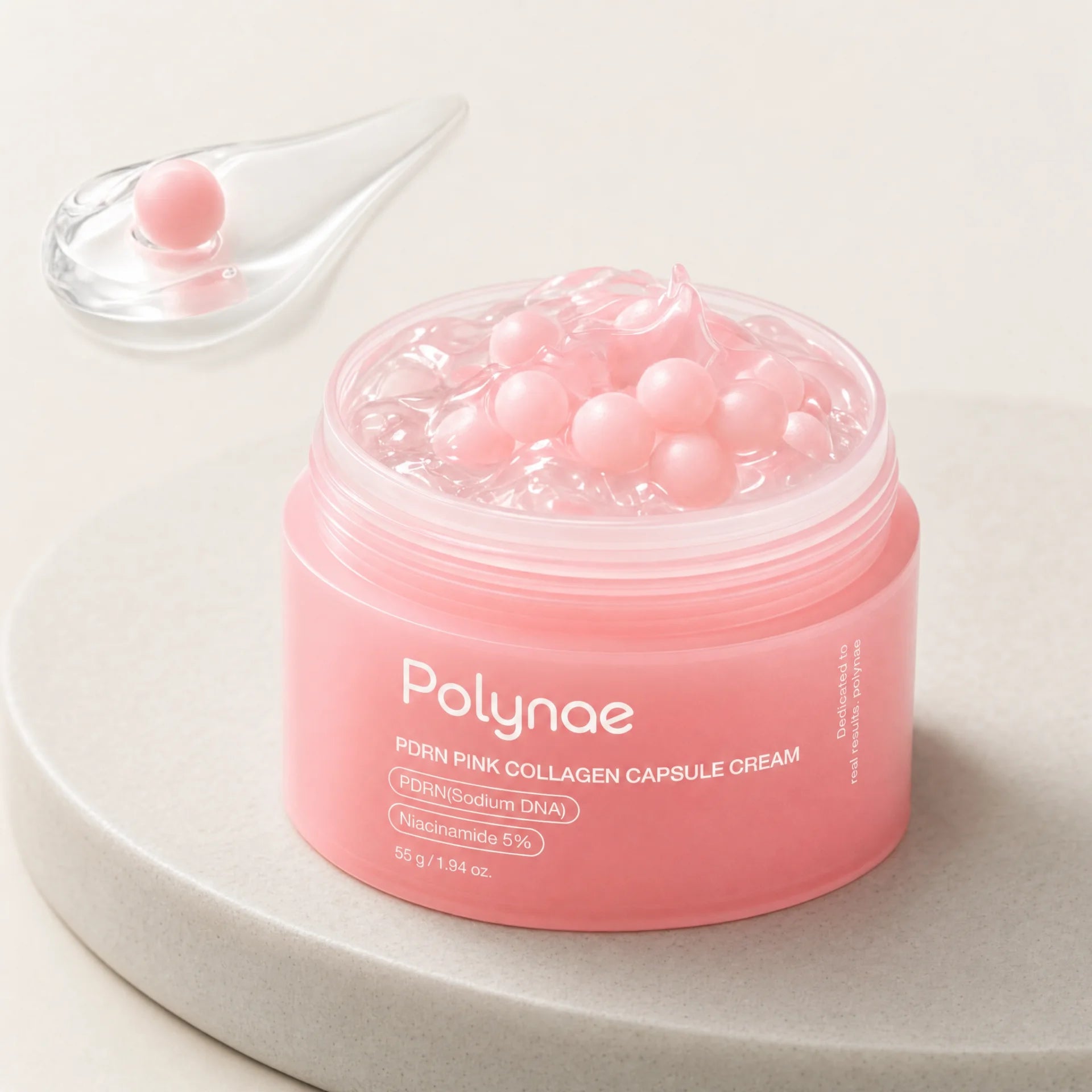 Open jar of Polynae PDRN Pink Collagen Capsule Cream showing pink gel base filled with pink spherical capsule beads, placed on a stone surface beside a glass co