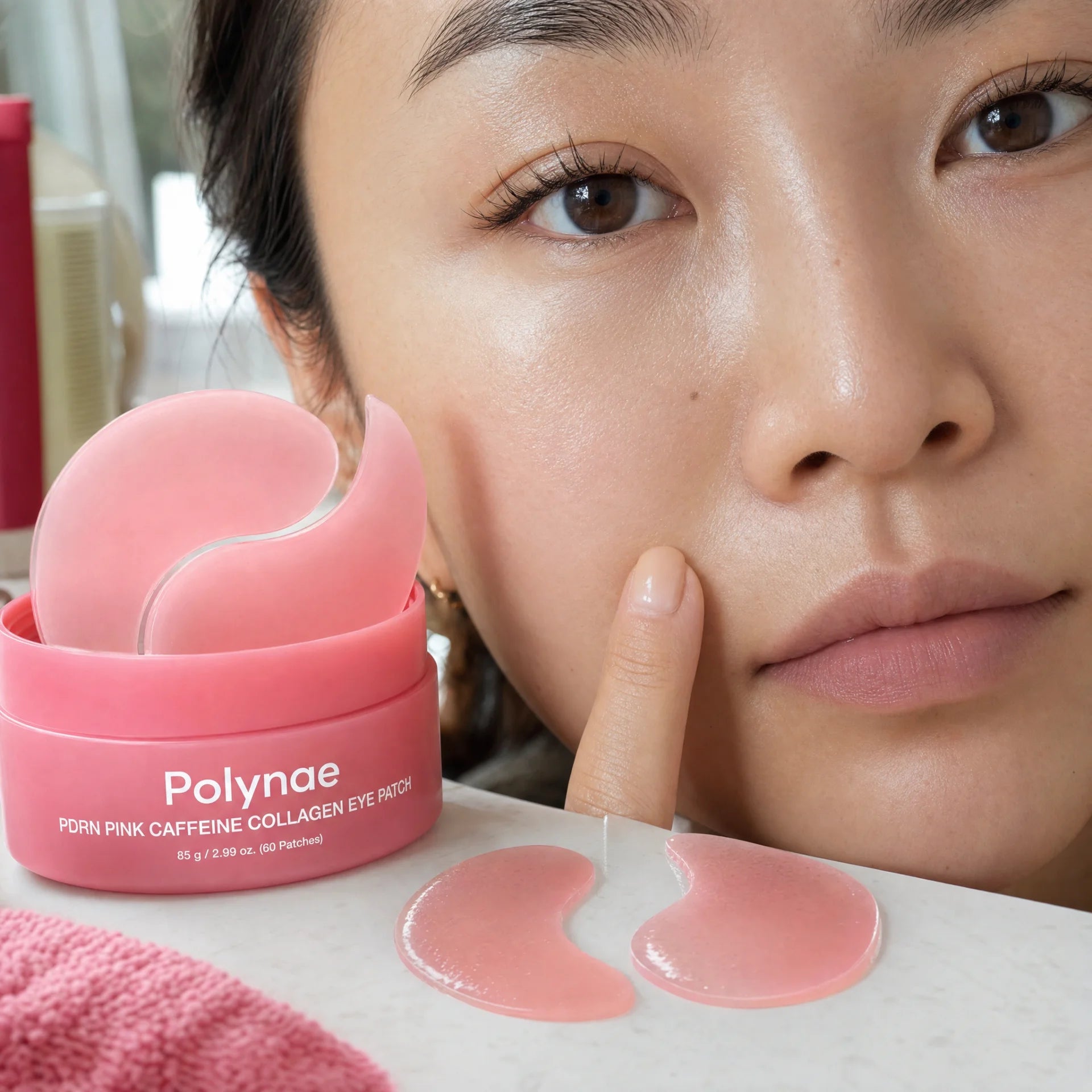 Asian woman with Polynae eye patches applied under both eyes, touching her cheek, with the open product jar on the surface beside her