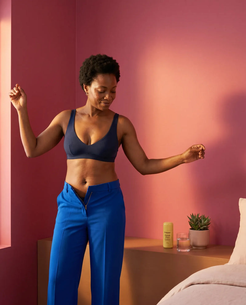 Woman dancing freely in a blue bra top and cobalt trousers with Polynae Fresh That Lasts deodorant visible on a nearby surface
