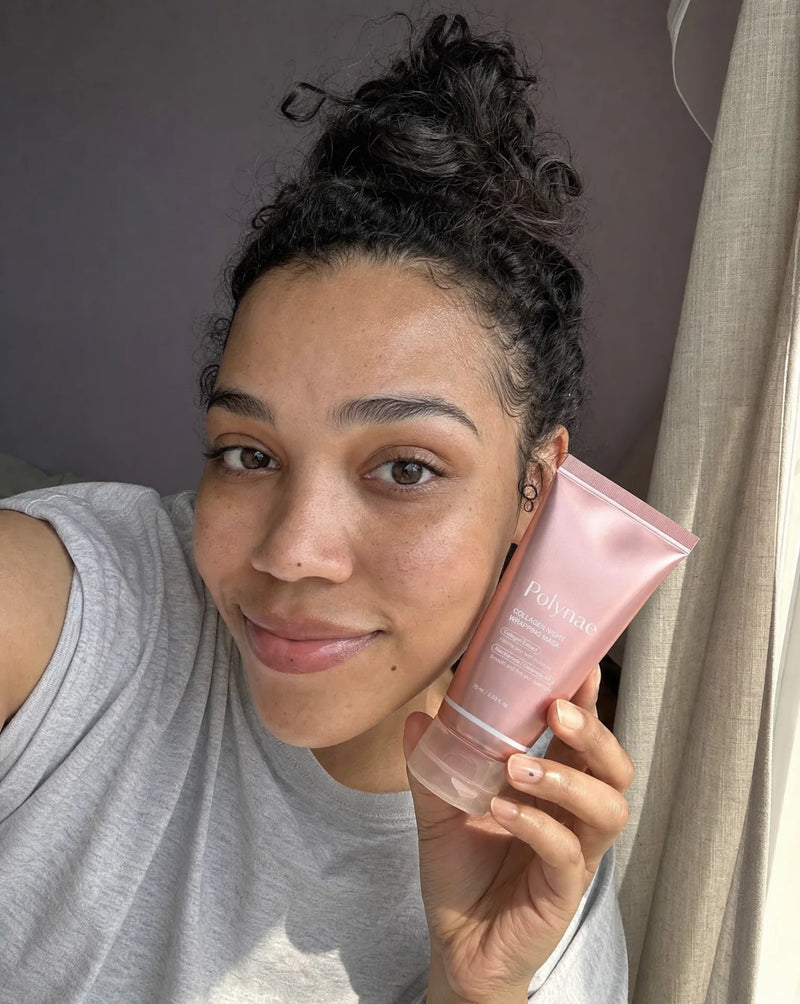Selfie of a woman with curly hair in a gray tank top holding the Polynae tube against her cheek, natural light, relaxed expression