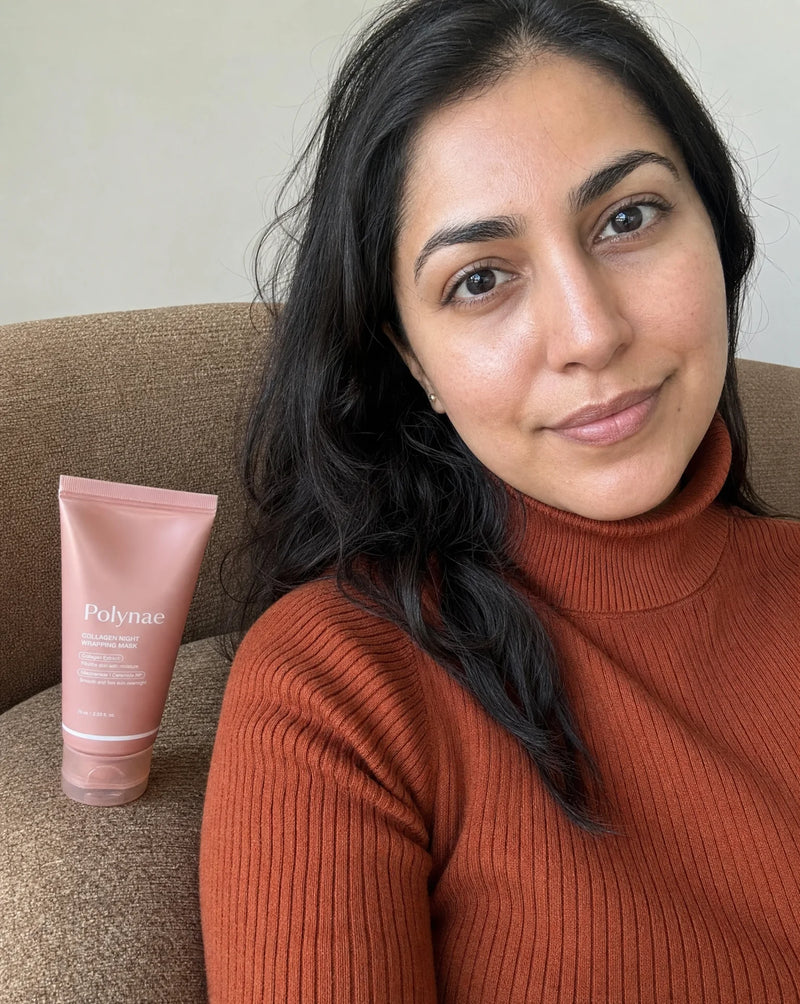 Woman in rust turtleneck seated on a beige sofa next to the Polynae tube and a small jar, clear healthy-looking skin, direct gaze