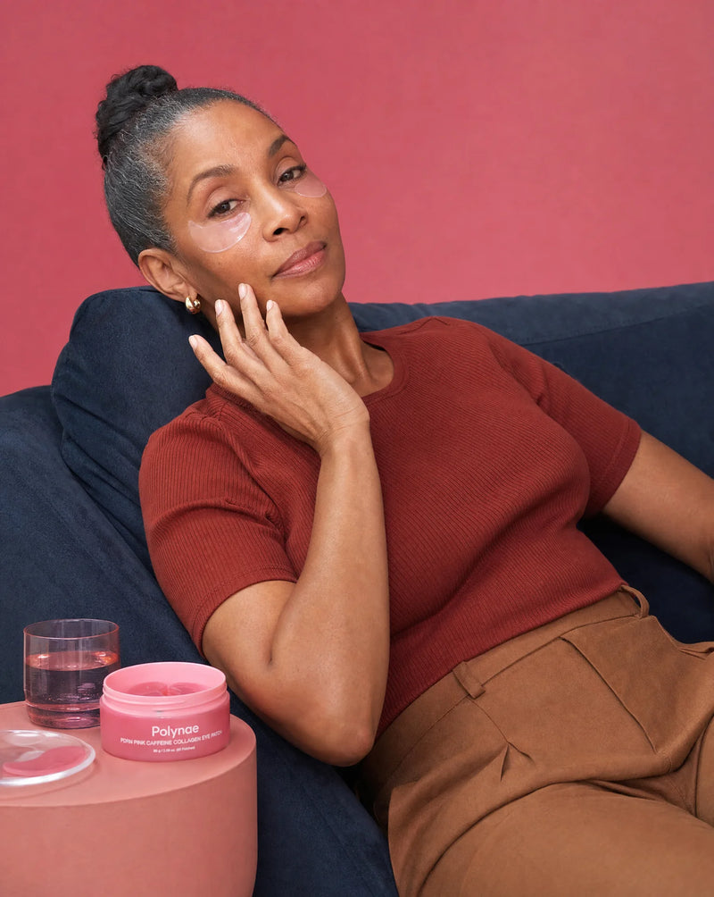 Woman relaxing on a sofa wearing Polynae pink eye patches, Polynae jar on a small table beside her