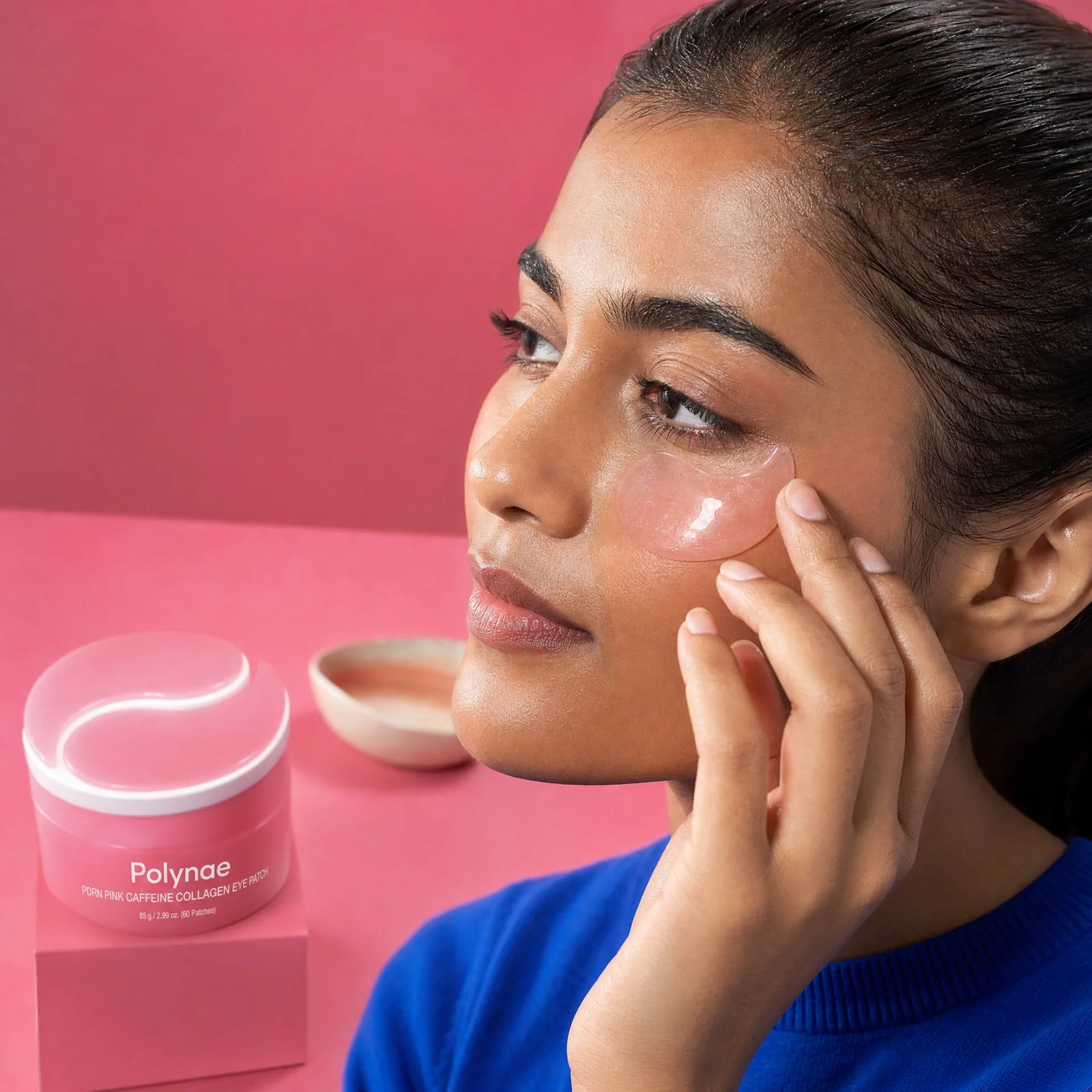 Close-up of a woman pressing a translucent pink Polynae eye patch against her under-eye area, Polynae jar in foreground