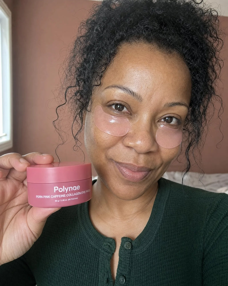 Casual selfie of a woman with curly hair wearing Polynae gel eye patches under both eyes, holding the product jar