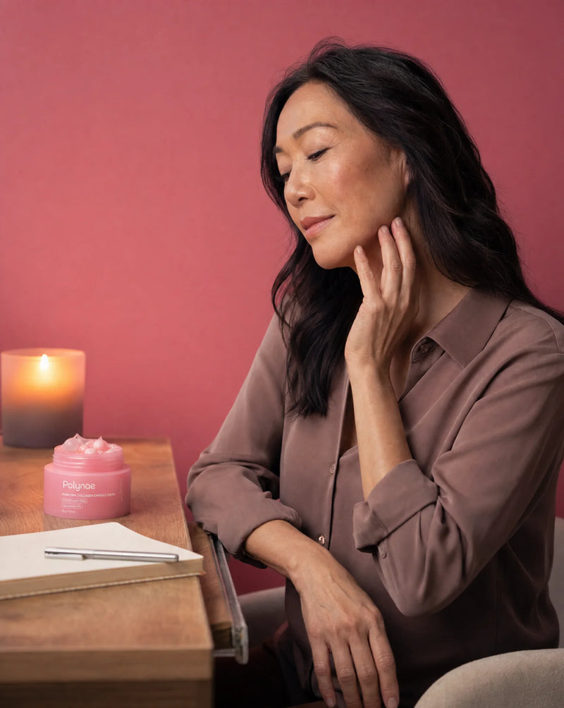 Woman in a taupe shirt touching her neck softly beside a lit candle and open Polynae cream jar