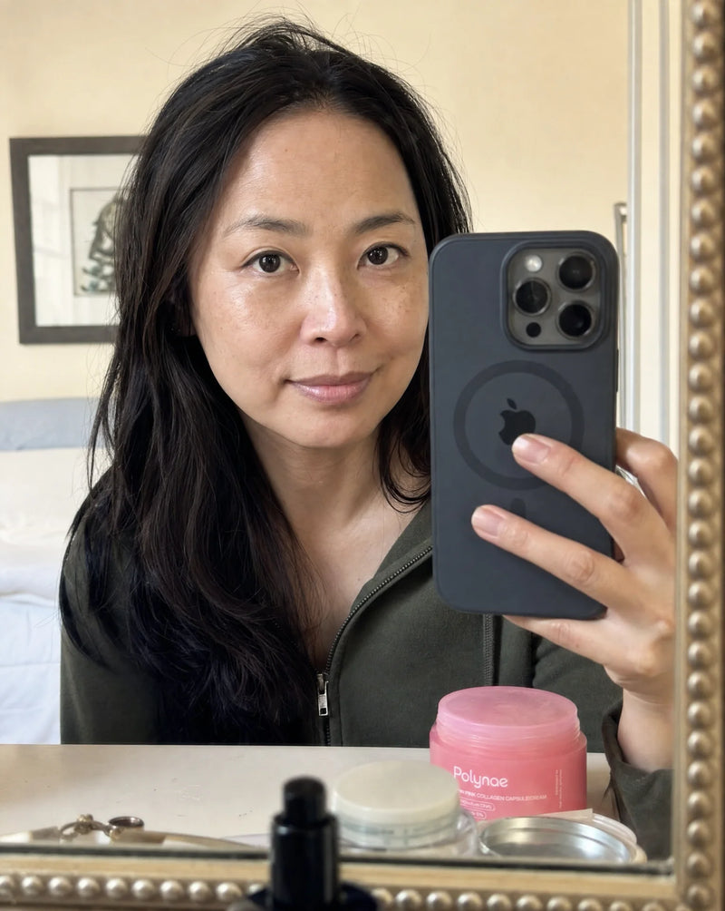 Mirror selfie of a woman with dark straight hair and even skin tone, Polynae jar on counter below