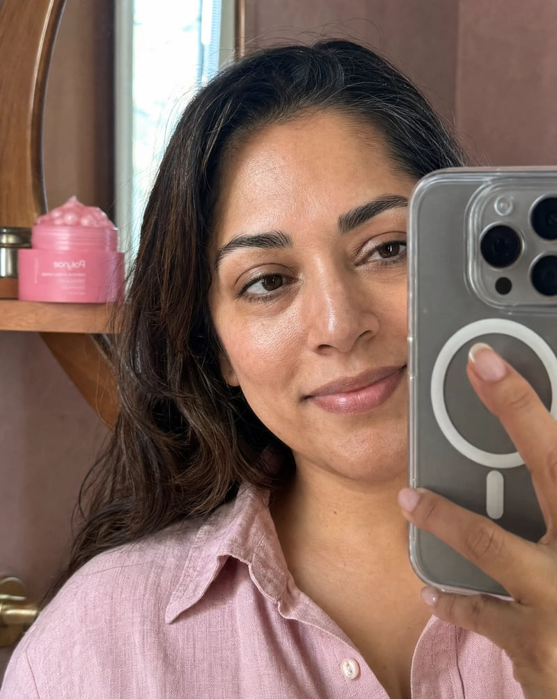 Woman taking a mirror selfie with Polynae pink jar on a shelf behind her, skin looking hydrated