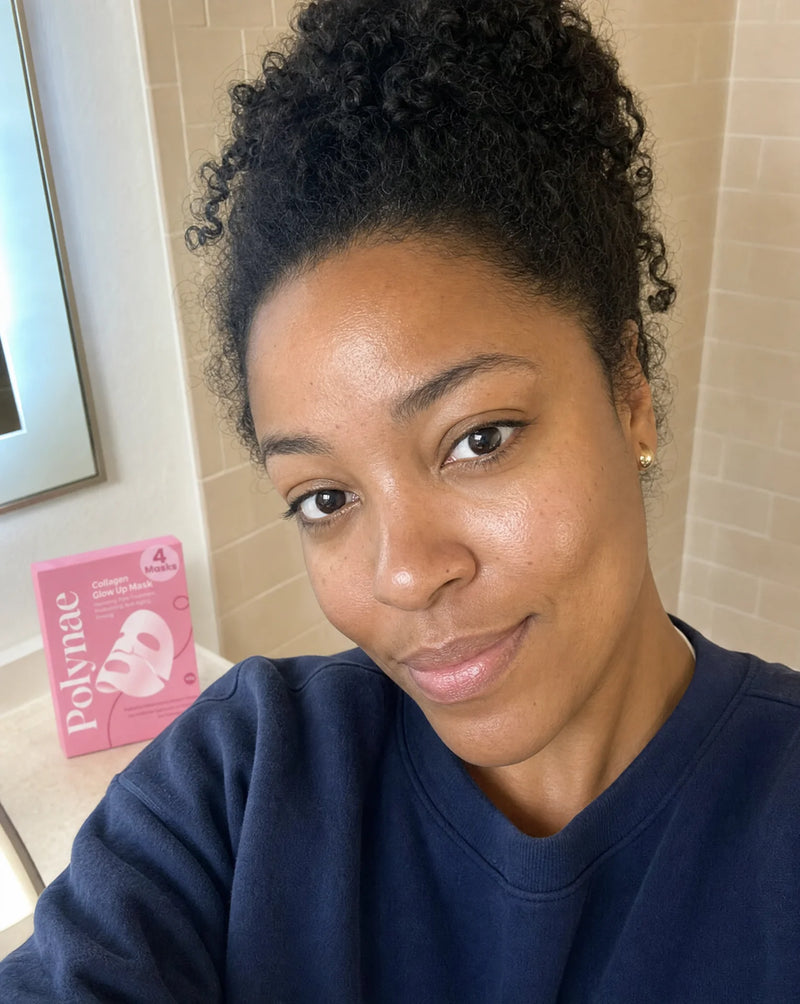 Woman with natural curly hair takes a bathroom selfie after using Polynae Collagen Glow Up Mask, pink product box visible on counter behind her