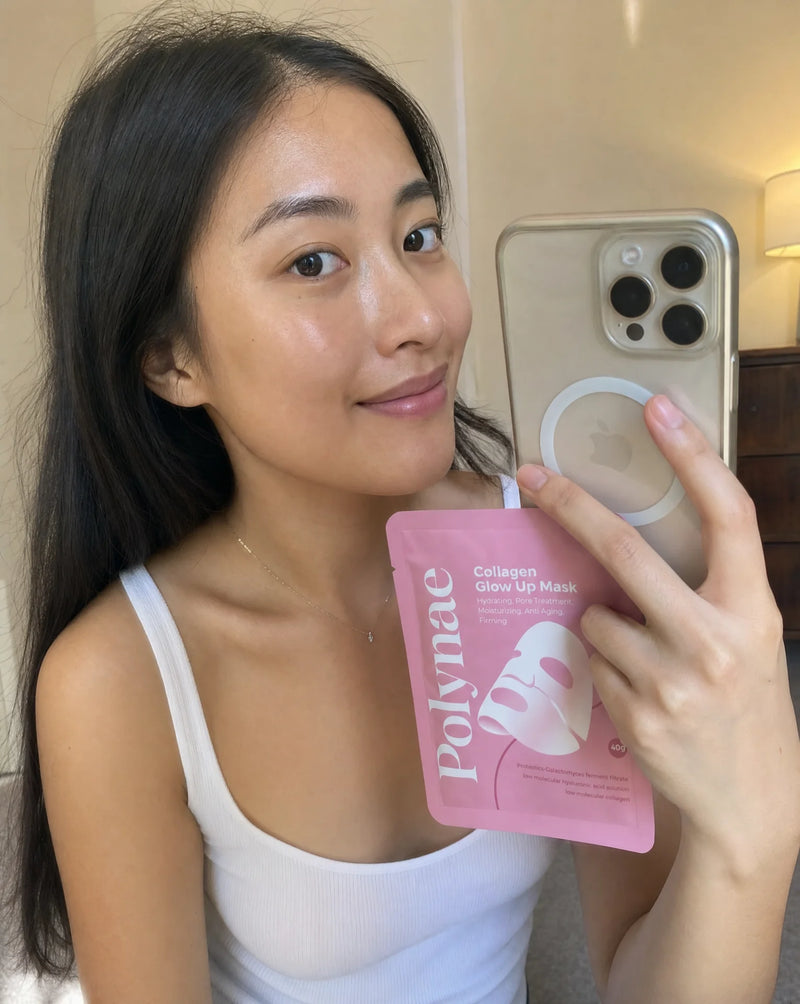 Mirror selfie of a woman holding a single Polynae Collagen Glow Up Mask packet, skin appearing dewy and fresh